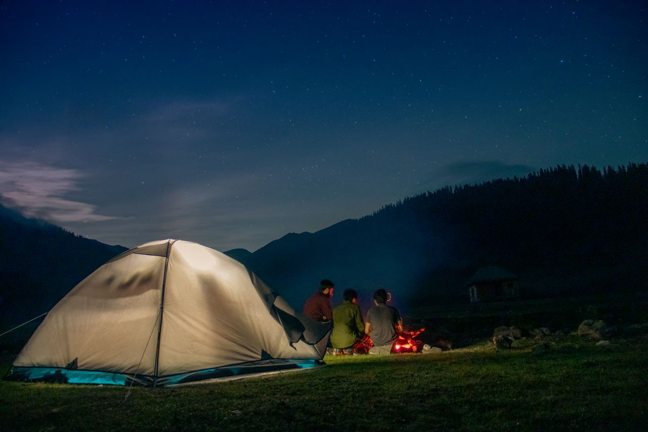 Group of adults camping with a cozy campfire at night in Bangus Valley, surrounded by starry skies.