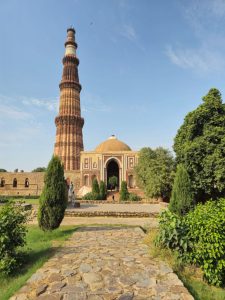 Breathtaking view of the Qutub Minar in New Delhi, framed by lush greenery and an ancient path.