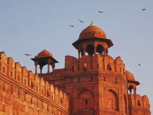 Close-up of Red Fort's intricate architecture at sunset with flying birds.